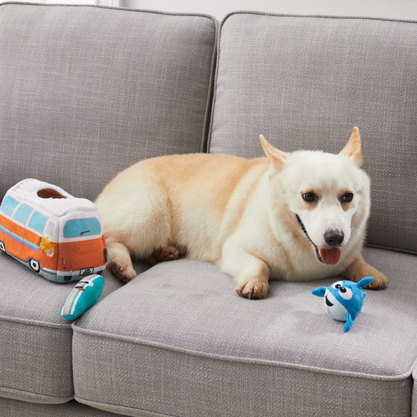 A happy pup surrounded by the Hide A Surf Van and plush squeaky toys, showing the fun and enrichment it provides.