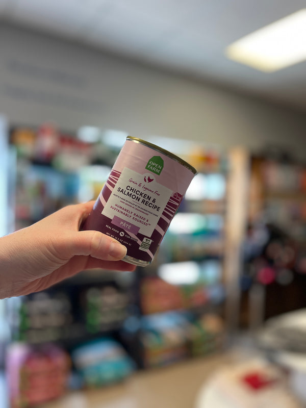 An image of a hand holding up the Open Farm Chicken & Salmon Pâté can, emphasizing its premium quality and the commitment to ethically sourced, nutritious ingredients for dogs.