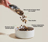 Scoop of nutrient-dense dog food falling into bowl with arrows pointing to benefits like multi-animal protein for muscle development, pumpkin for digestion, and freeze-dried raw coating for enhanced flavour and nutrition