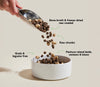 Action shot of protein-rich kibble and freeze-dried raw chunks being poured into a dog bowl, with arrows highlighting benefits like muscle support from diverse proteins, improved digestion from superfoods, and enhanced palatability from bone broth coating