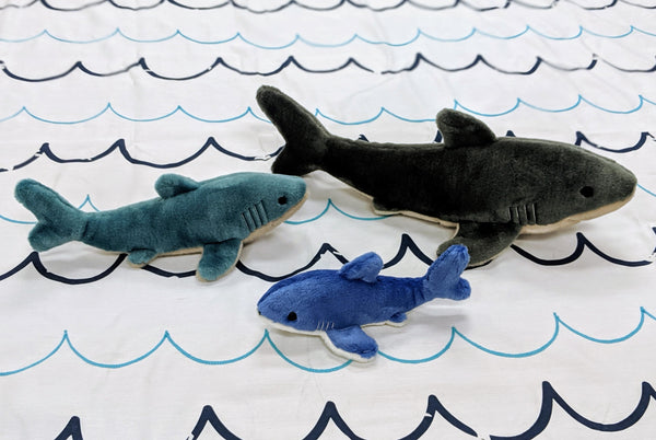 Fluff & Tuff Shark Family size comparison featuring Mac the Shark (Large), Tank the Shark (Small), and Baby Bruce the Shark (Extra Small), showcasing the range of plush shark dog toys available for different breeds, play styles, and life stages, all crafted with ultra-soft fabric, reinforced Tuffweb™ mesh lining, embroidered safety details, durable construction, and machine-washable materials for fetching, carrying, cuddling, and interactive play.