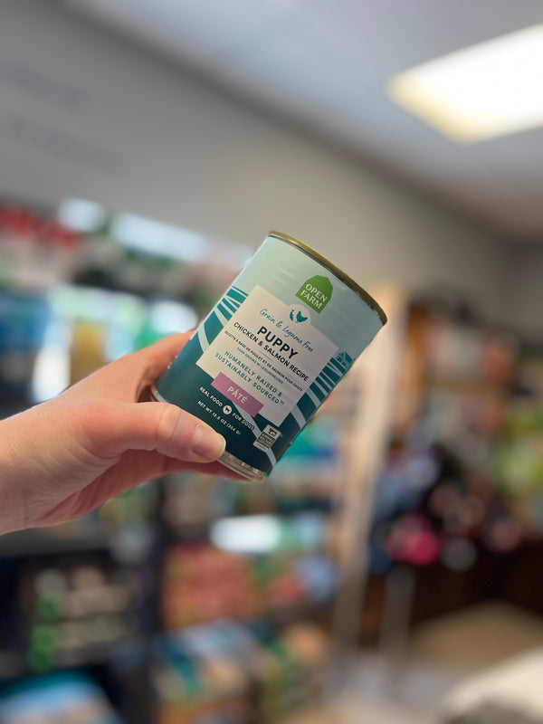 An image of a hand holding up the Open Farm Chicken & Salmon Pâté for Puppies can, emphasizing its premium quality and the essential nutrients for supporting puppy growth and development.